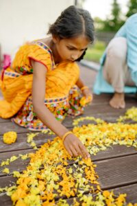 pexels photo 8818738 8818738 South Asian girl arranging petals in traditional clothing on a wooden deck during a festival.